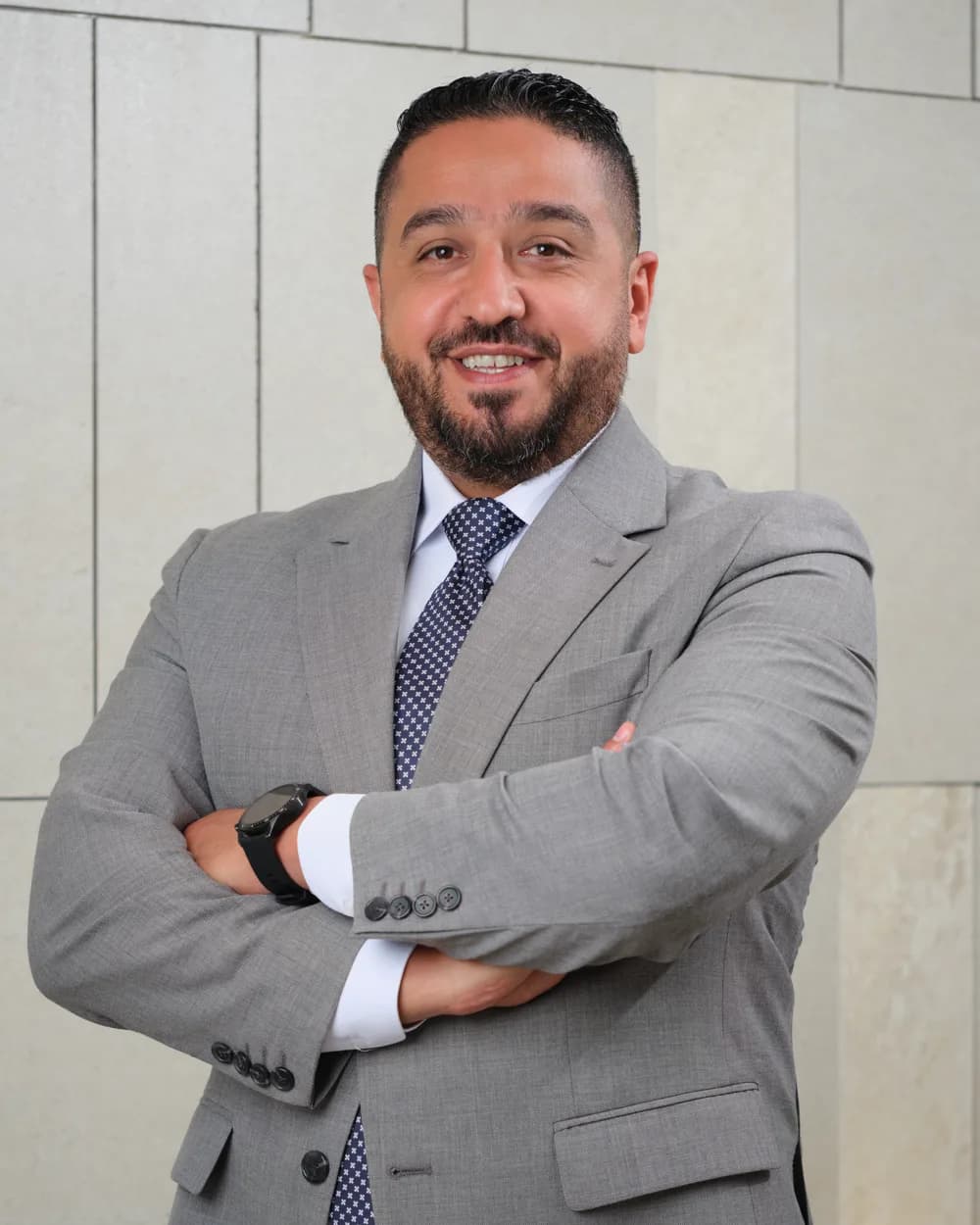 Ammar Sa'ad in a grey suit, arms crossed, against a stone-tiled wall