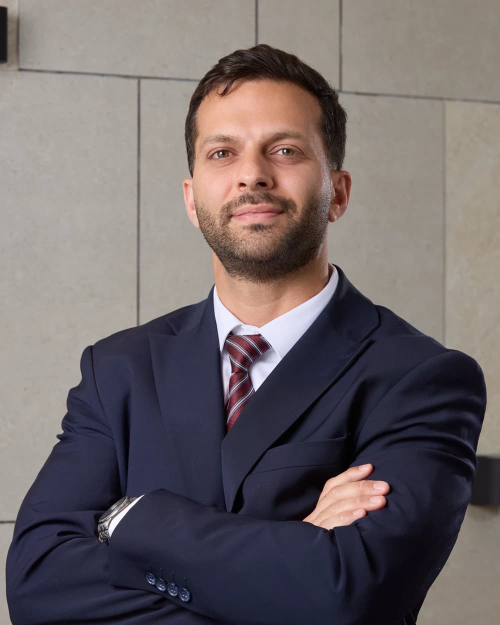 Faris Haddad in a navy suit and red tie, arms crossed, against a stone-tiled wall